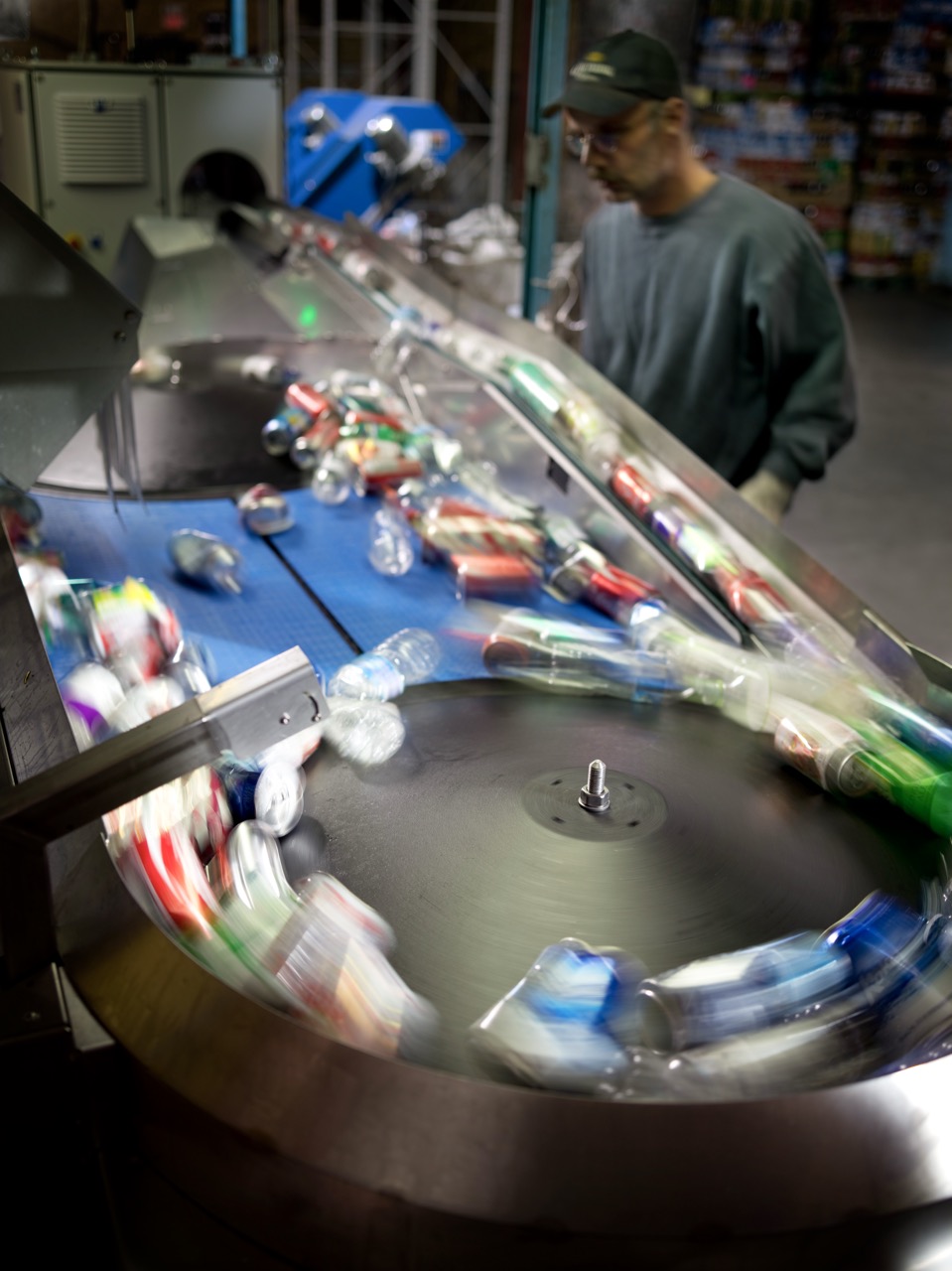 A worker sorting empty beverage containers on a moving conveyor