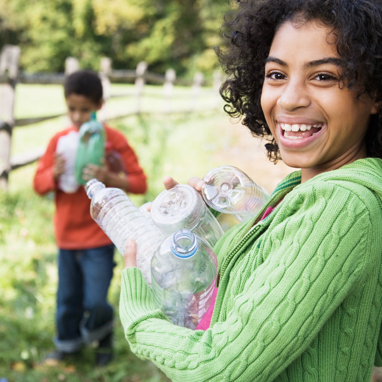 A smiling girl holding an armful of empty plastic bottles